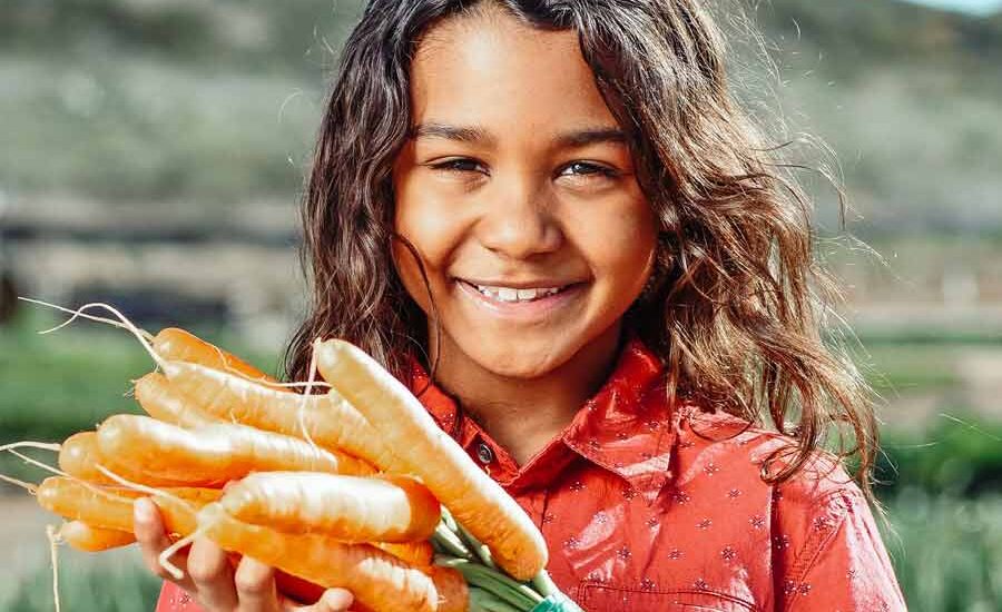 Gadis kecil menujukkan wortel yang siap dimasak (foto: Kindel Media | pexels)