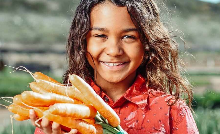 Kampanye Makan Sehat di Berbagai Negara, Seperti Apa Sih? Gadis kecil menujukkan wortel yang siap dimasak (foto: Kindel Media | pexels)